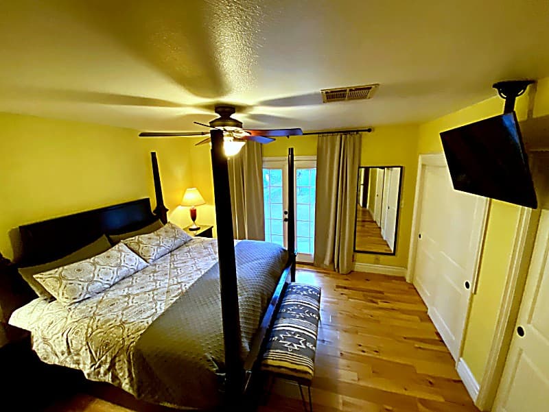Primary bedroom with a four-poster king bed, wall-mounted TV, and French doors to the backyard
