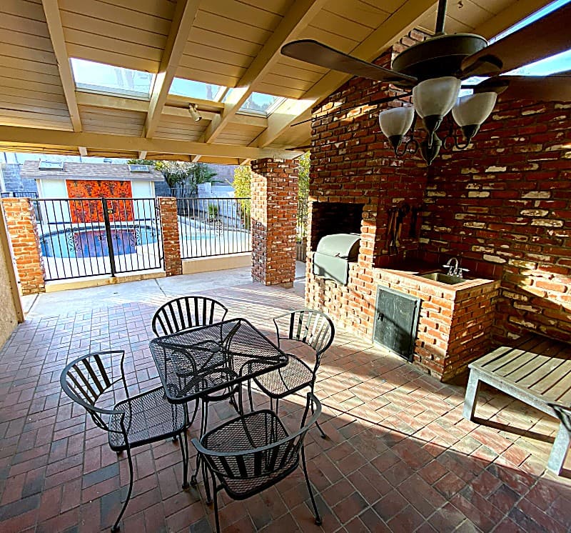 Large covered brick patio with built-in charcoal grill, sink, and a four-top table by the pool