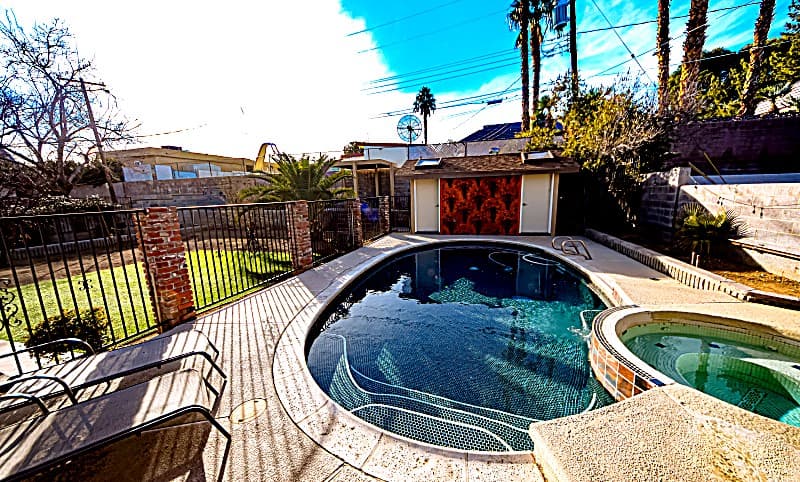 Oval pool and tiled in-ground hot tub in the fenced backyard with palm trees